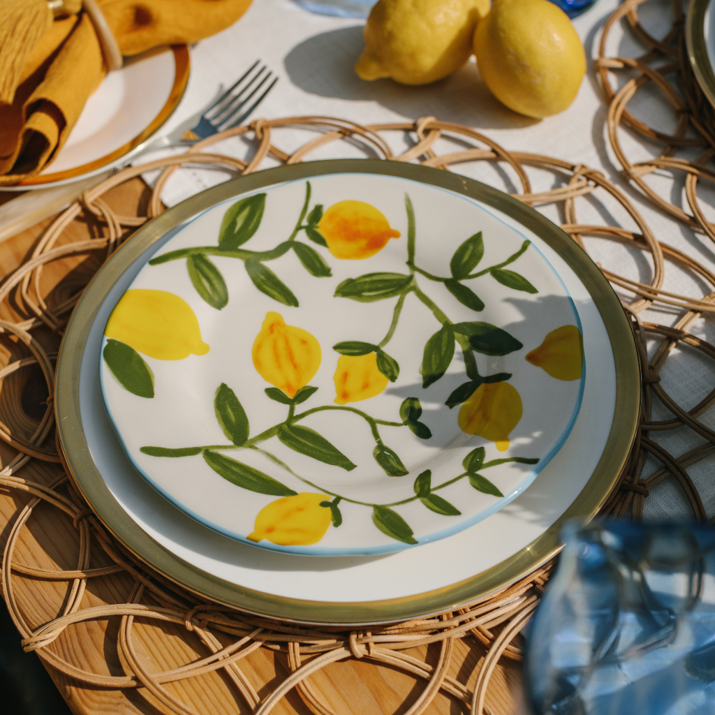 Yellow lemon plate with green twig detail set on gold trim main plate on a woven rattan placemat