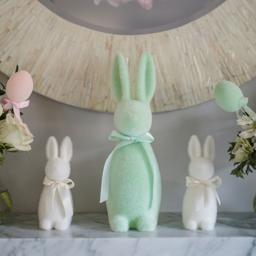 Large mint green flocked Easter bunny decoration standing on a white marble mantle between two small cream Easter bunny twin decorations