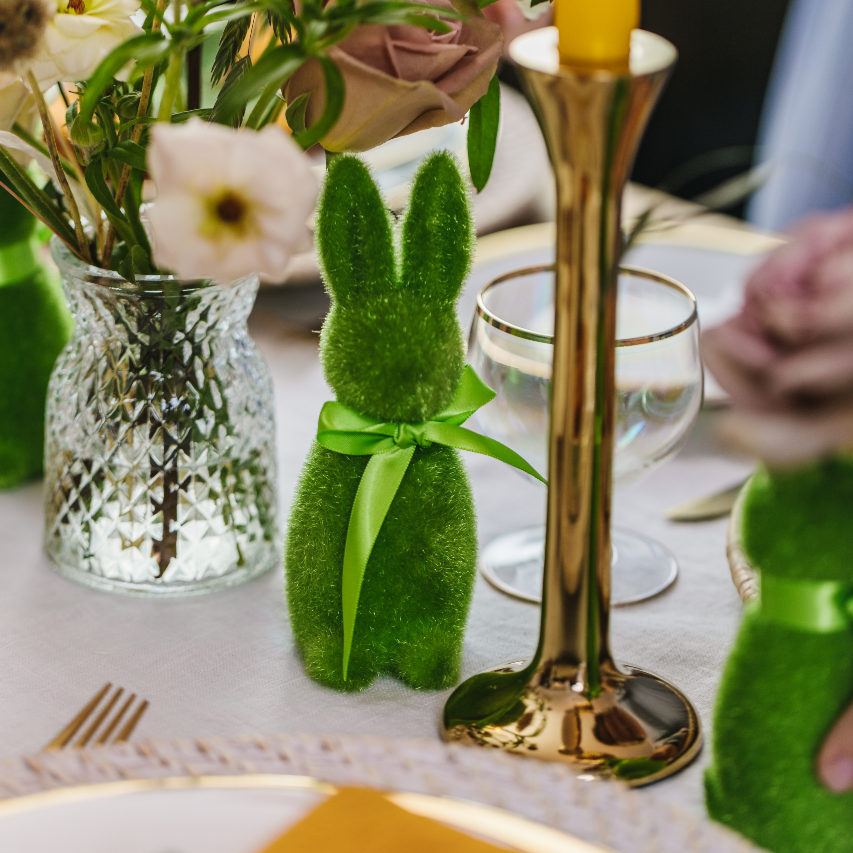 Moss green flocked easter bunny standing decoration on a table centre next to a brass candlestick and cut glass bud vase.