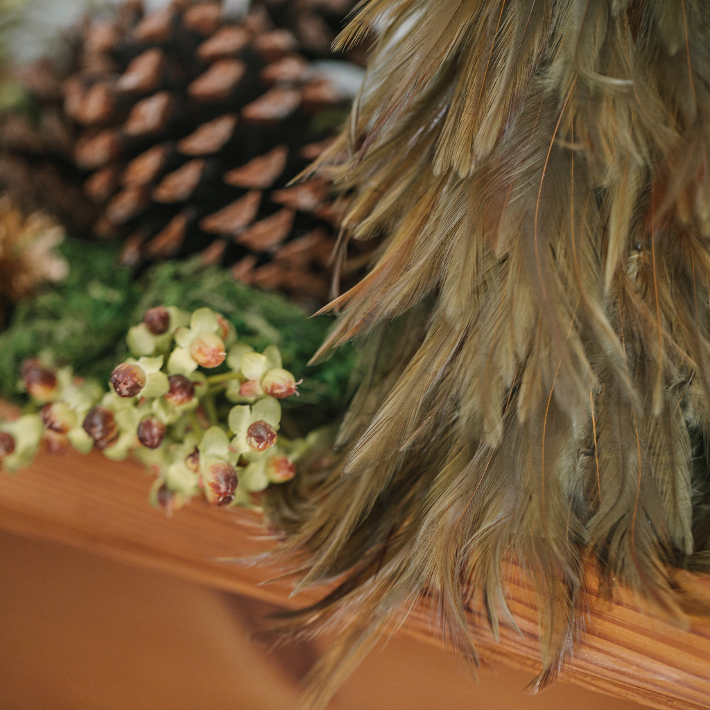 Close up of feathers on Christmas tree decoration next to festive foliage and pine cones