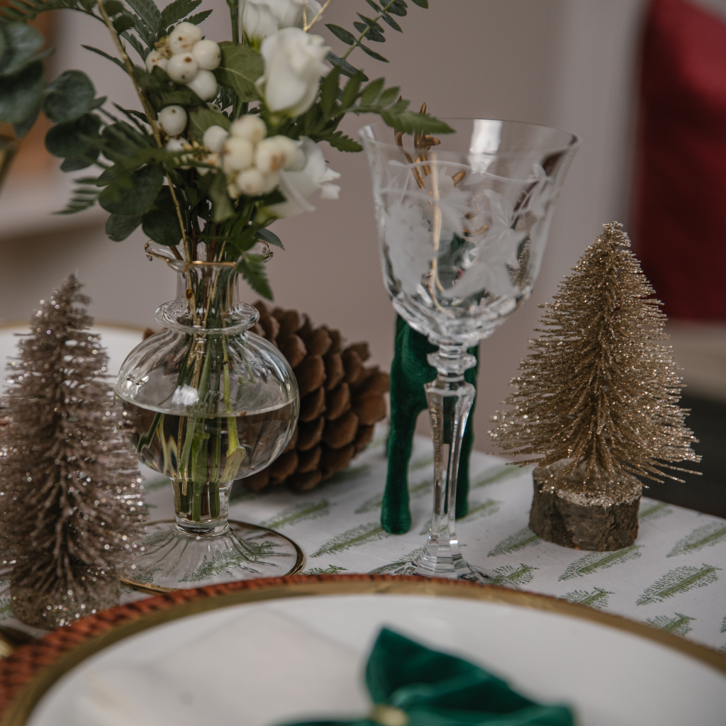 Tabletop with wine glass next to gold glitter brush tree on wooden base and gold trimmed bud vase