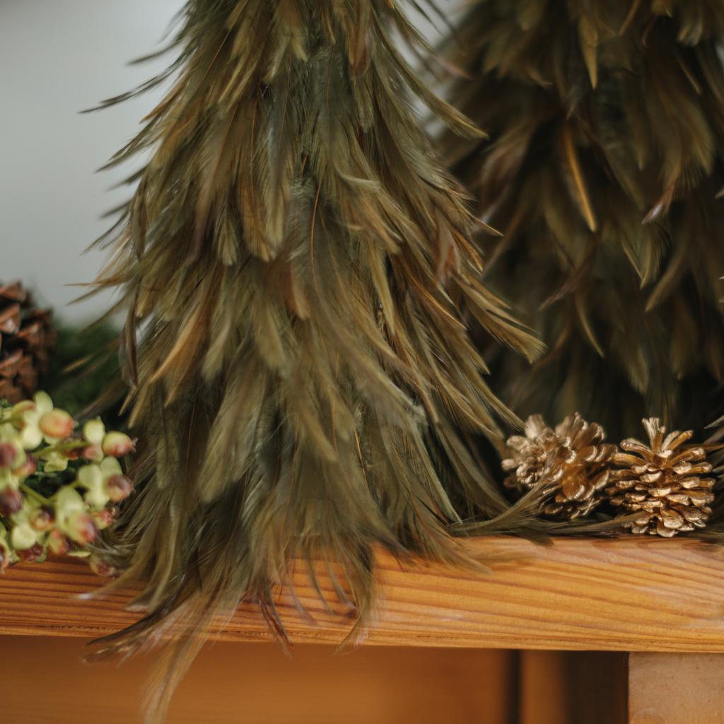 Close up of lustrous green feathers of festive decoration next to gold pine cones