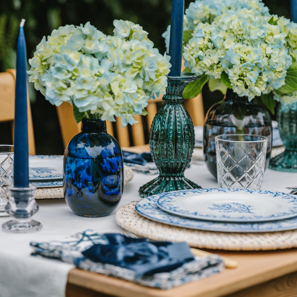 The Santorini coral tablescape with blue leopard glass vases, white table runner, blue coral plate sets and navy tapered candles in aquamarine glass holders