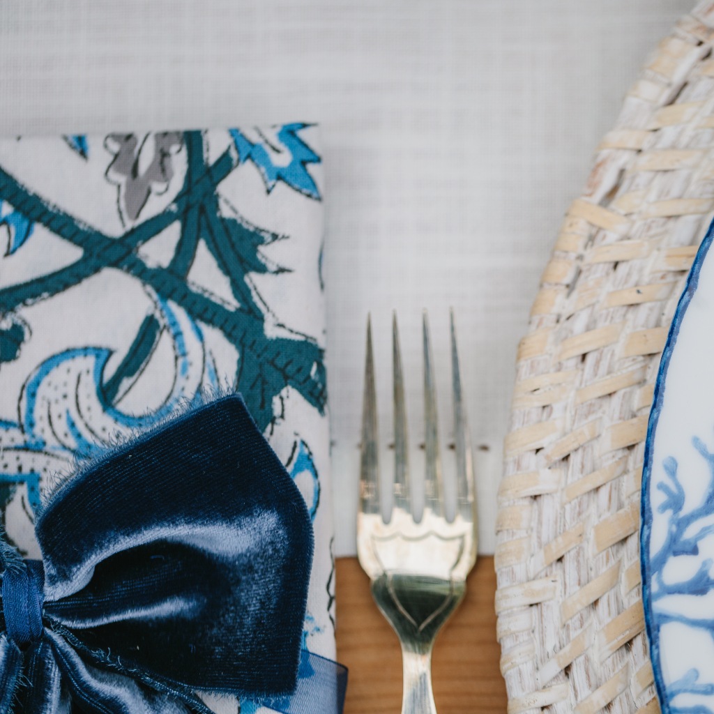 Close up of navy, kingfisher blue and white Santorini block printed napkins, navy napkin bows and white rattan charger plate