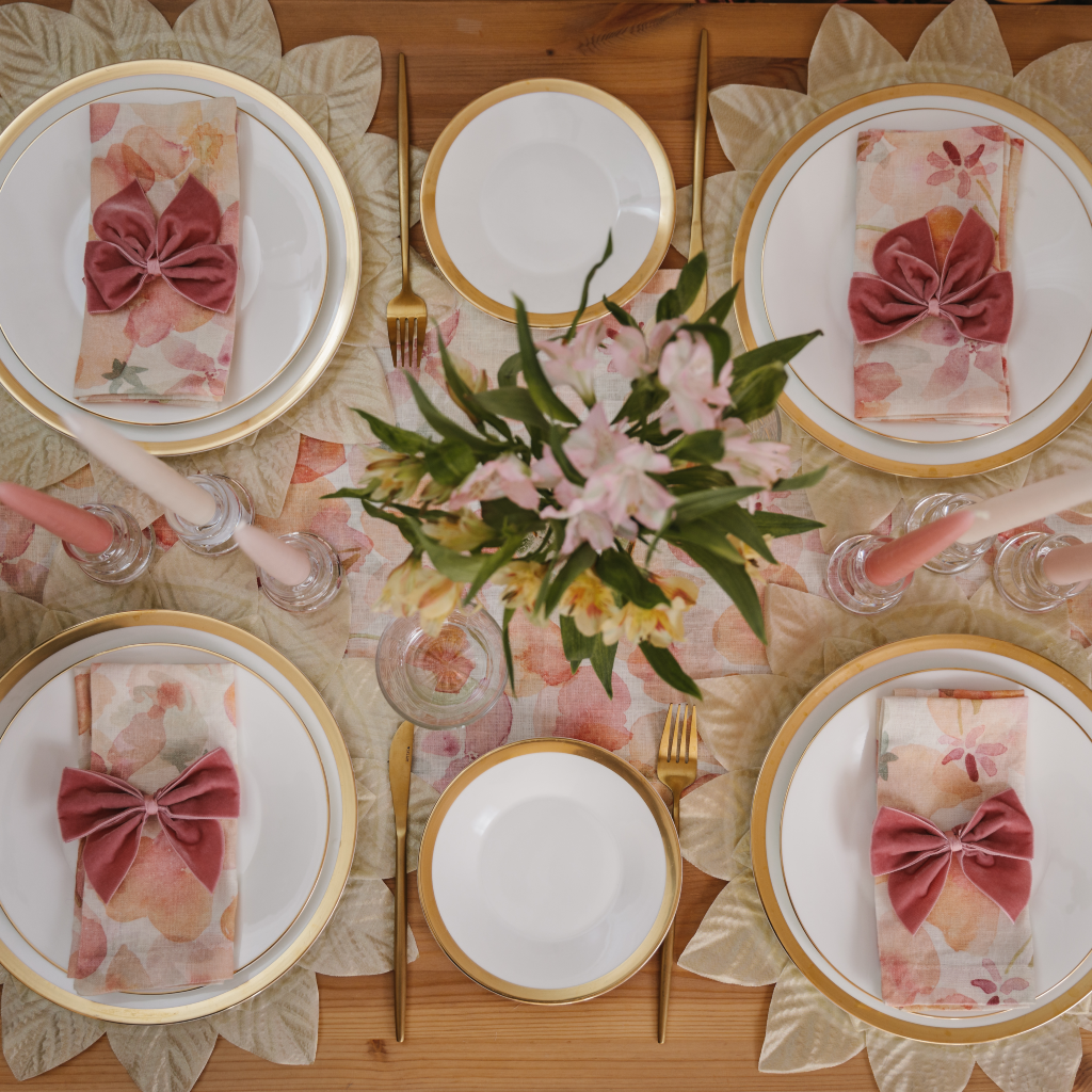 The Peaches and Cream tablescape set for four people including linen table runner, pink tapered candle trios, flower posy and gold and pink place settings finished with gold trimmed crockery and gold cutlery