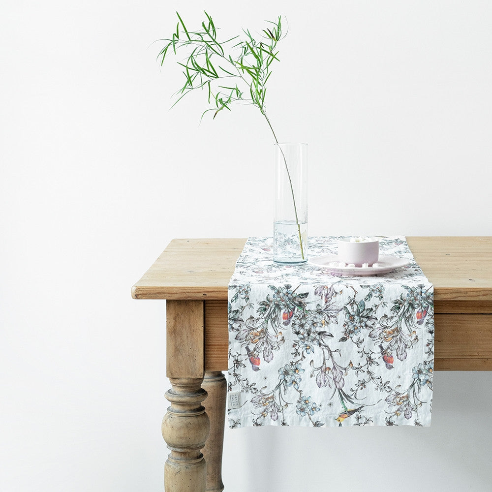 Wildflower Garden Table Runner on rustic table with an individual clear vase displaying greenery and a white sugar dish and plate.