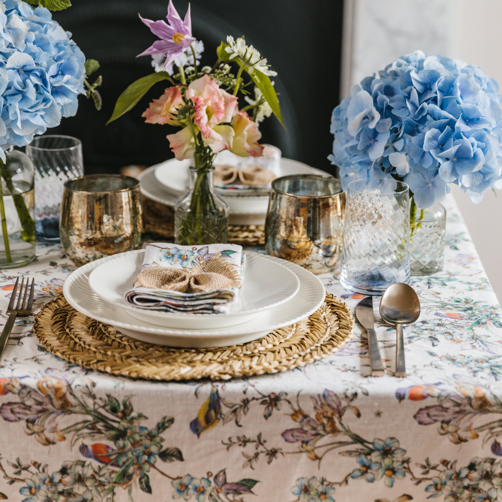 Side on view of spring wildflower tablescape including patterned table linen, copper tealight holders and clear bud vases containing wildflower selection.