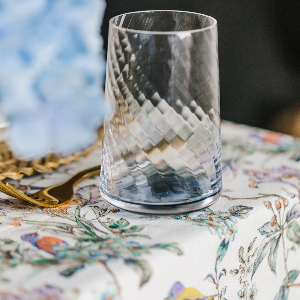 Blue rippled glass from Denby Porcelain Collection set next to gold fork on a 100% linen bird and flower print tablecloth.