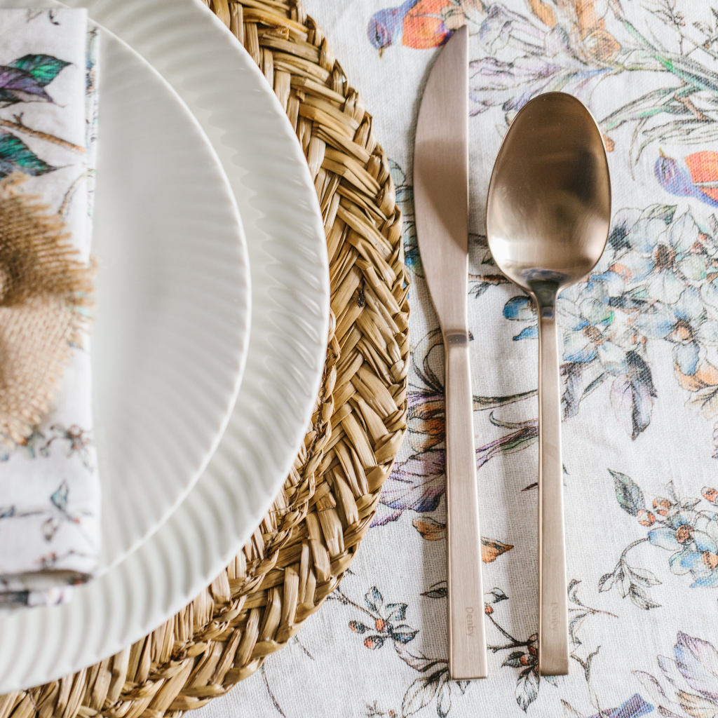 Close up image of wildflower pattern on 100% linen table runner. Seagrass placemat and Denby champagne gold crockery also feature.