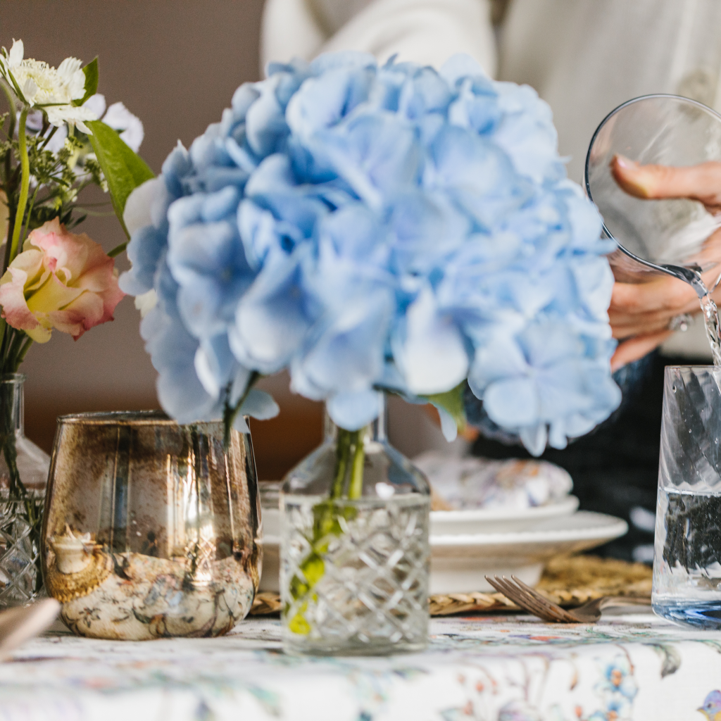Large blue hydrangea flower displayed in cut glass bud bottle next to a copper burnished candle holder. 
