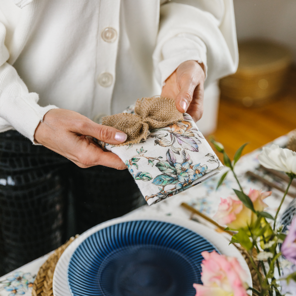 Hands tying a hessian napkin bow round wildflower printed linen napkin.